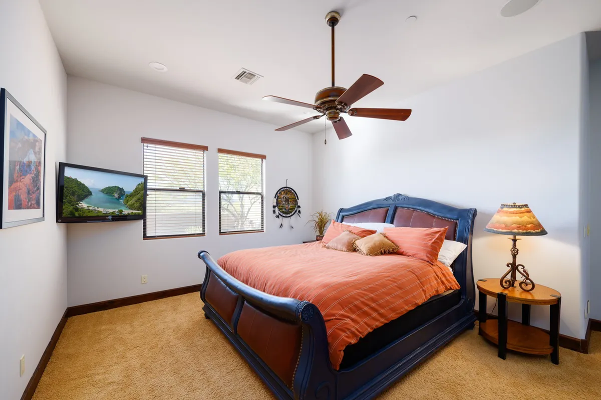 A guest bedroom with a large bed adorned in colorful bedding, a decorative lamp on the bedside table, and a mounted television for private entertainment. The room is styled for both comfort and functionality, ideal for restful nights and easy mornings.