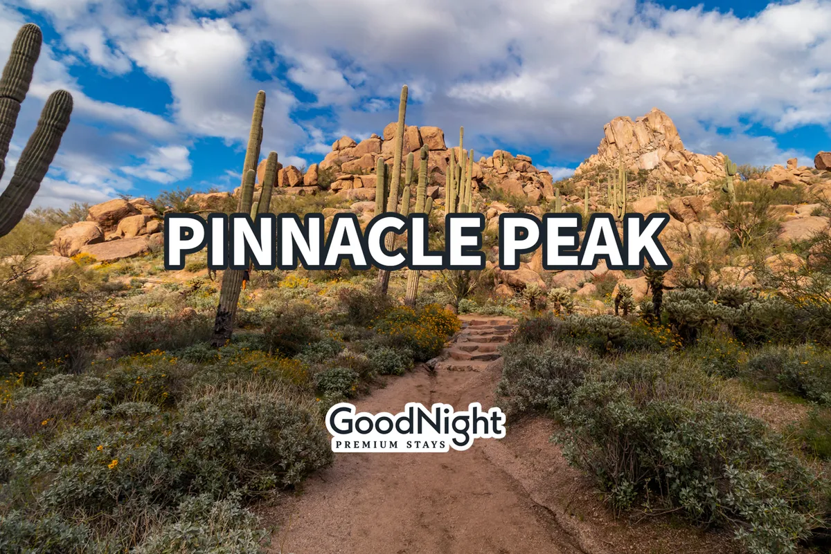 A scenic desert landscape featuring the iconic Pinnacle Peak, surrounded by rugged rock formations and native cacti, with a well-defined pathway inviting exploration. The setting is ideal for hiking and adventure.