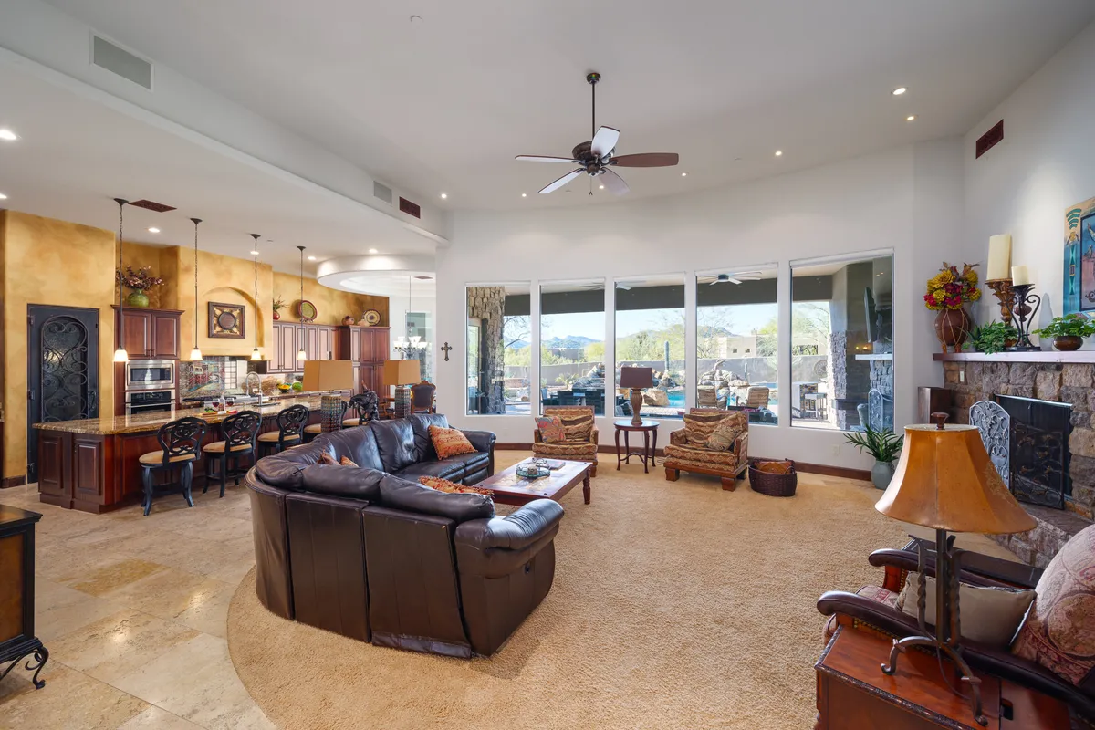 A welcoming open-concept space featuring a large sectional sofa, a central fireplace, and a dining area in the background. Expansive windows reveal a scenic mountain view, bathing the room in natural light. The arrangement is ideal for both relaxing by the fire and hosting gatherings around the dining table.