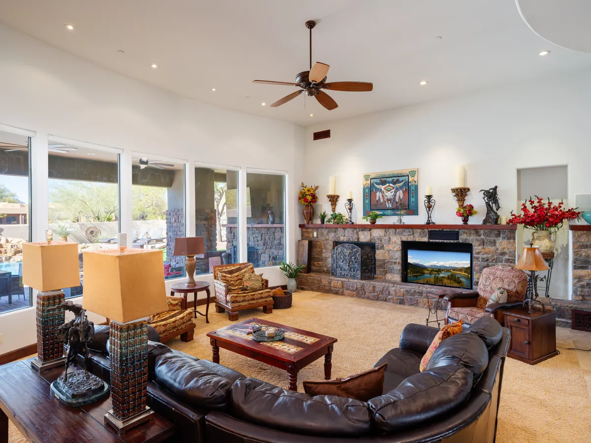 A spacious and cozy living area with a stone fireplace as the focal point, surrounded by large windows letting in ample natural light. Comfortable seating is arranged for socializing, and decorative artwork adds a touch of luxury. The room exudes warmth and is perfectly designed for families or groups to gather for relaxing or entertaining.