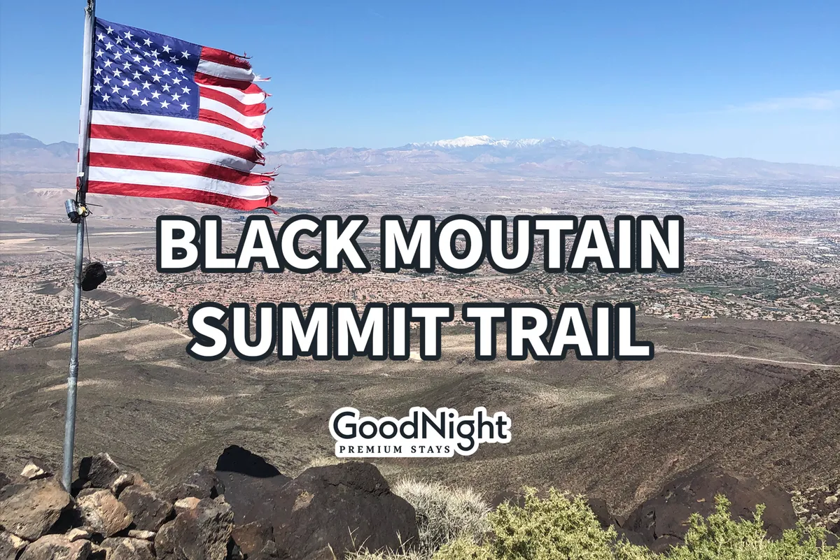 An inspiring panoramic view from a mountaintop features an American flag, a sweeping valley below, and a mountain range in the distance. The vantage point suggests the payoff from a rewarding hike or outdoor adventure.