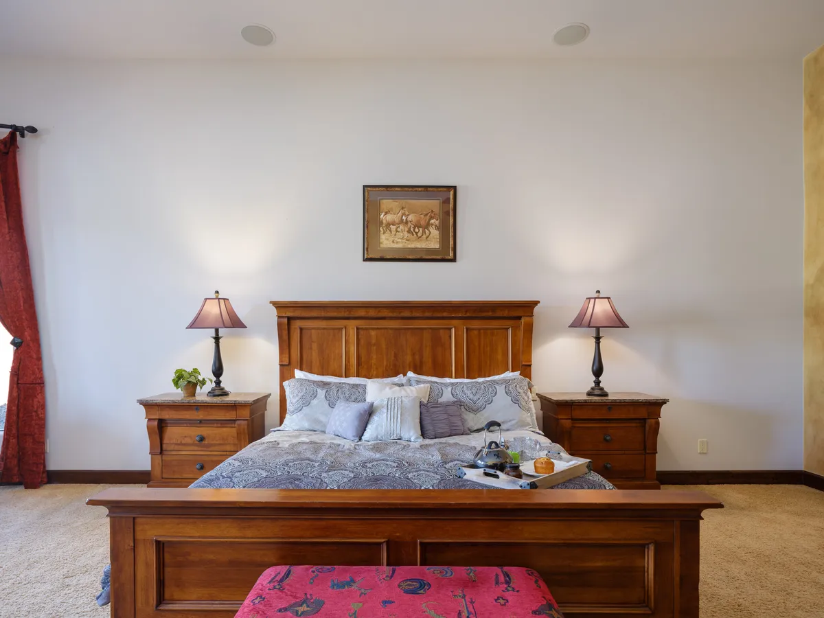 A well-appointed bedroom featuring a wooden bed frame, decorative pillows, and nightstands with lamps. Framed artwork and natural light streaming in add to the cozy, restful atmosphere, making it adaptable for various sleeping arrangements including air mattresses or a pack & play.