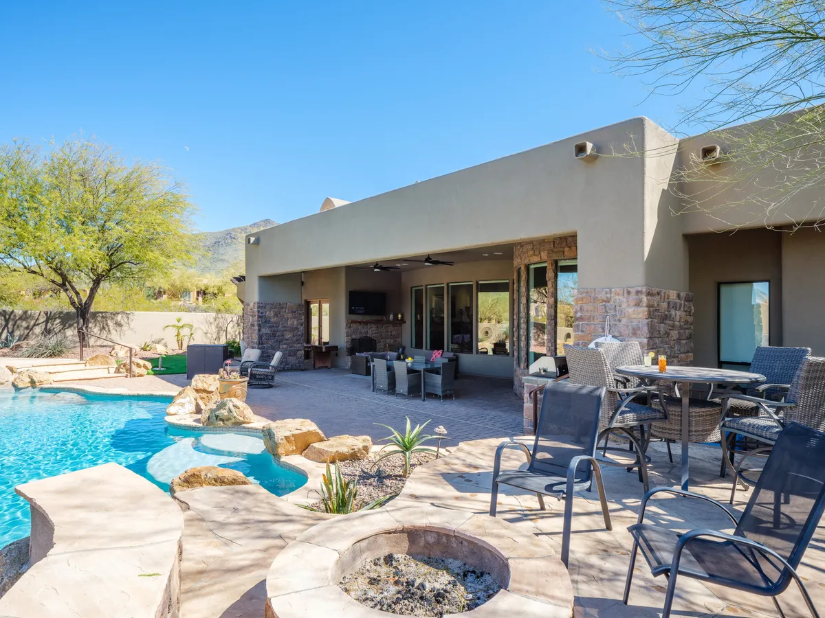 A stunning backyard scene with a sparkling swimming pool, outdoor lounge seating, a modern fire pit surrounded by chairs, and lush landscaping. The area is designed for both daytime relaxation and evening gatherings, with ample space for al fresco dining and socializing by the fire.