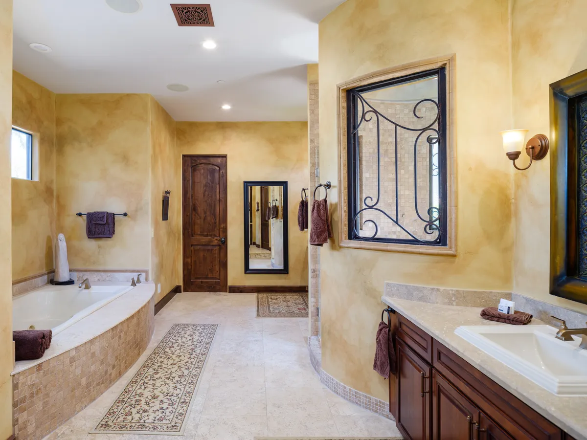 A serene bathroom featuring a deep soaking bathtub, a stylish vanity, and a window with decorative ironwork that lets in natural light. The design invites guests to relax and enjoy rejuvenating moments of self-care.