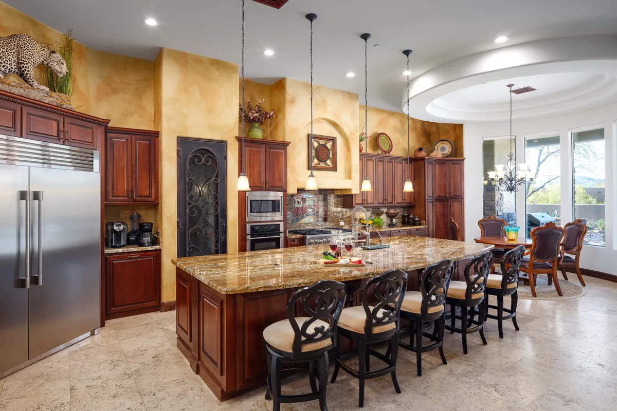 A modern, luxurious kitchen with a large granite island at its center, surrounded by top-of-the-line stainless steel appliances and elegant lighting fixtures. Decorative touches on the shelves add personality while the spacious layout encourages both cooking and social interaction.