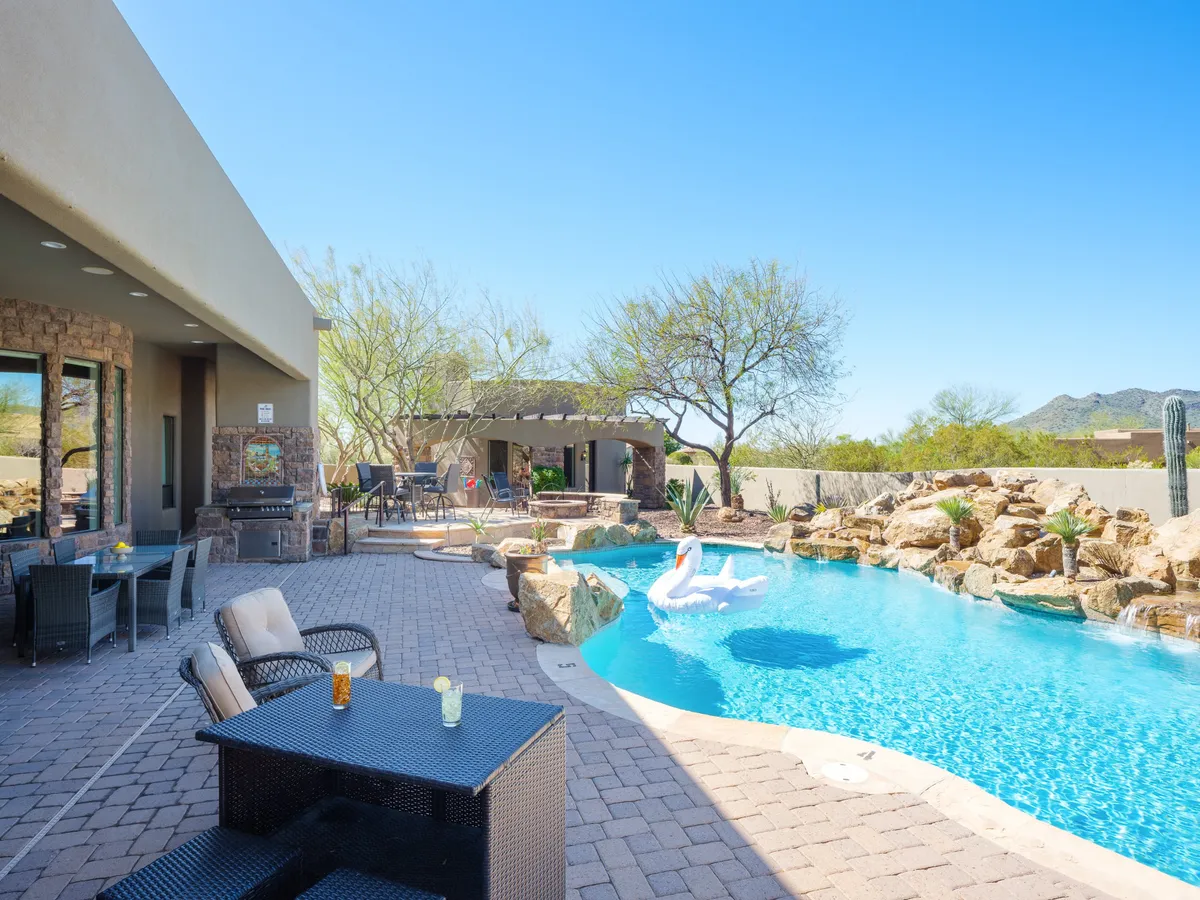A luxurious outdoor area showcases a sparkling swimming pool surrounded by comfortable lounge seating and landscaped rocks. An outdoor pergola sits beside the pool, with ample space for sunbathing, socializing, and enjoying starlit evenings. The tranquil setting is highlighted by soft, natural light, ideal for both day and night relaxation.