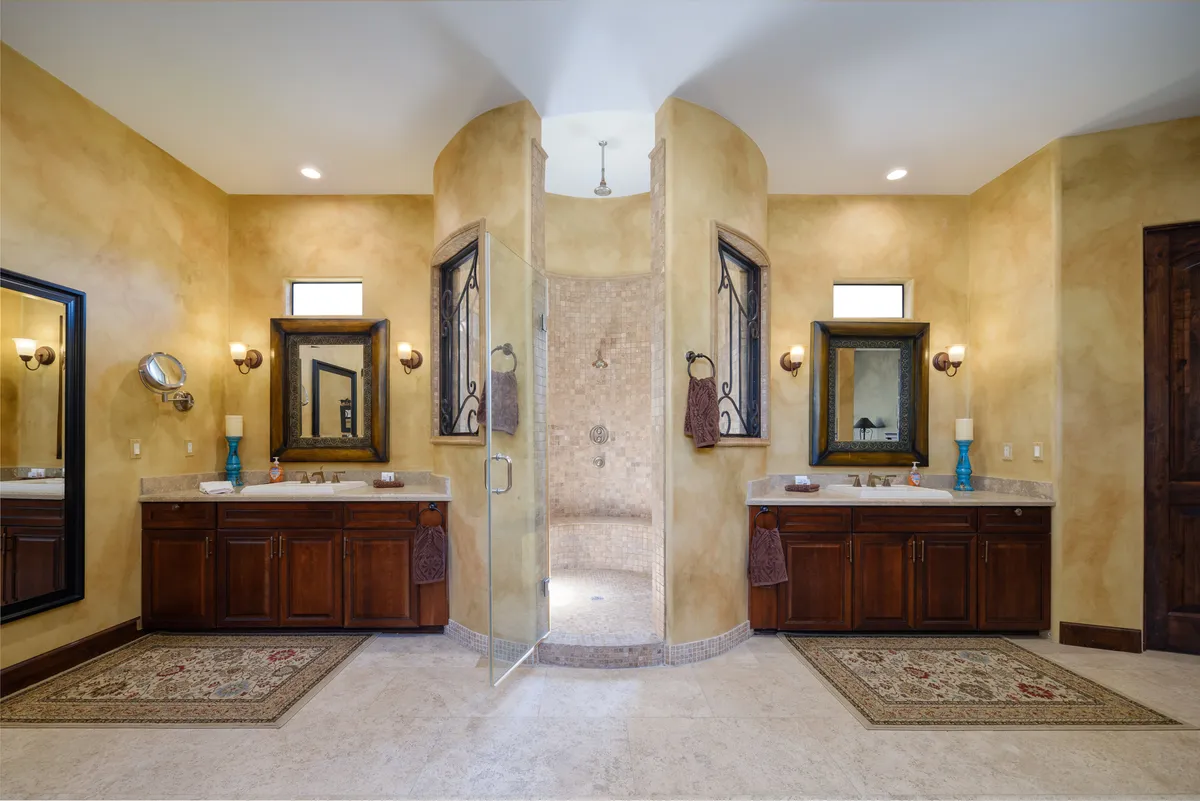 A luxurious bathroom with double vanities, a spacious walk-in shower, elegant decorative mirrors, and ornate rugs. The space radiates a spa-like ambiance, encouraging self-care and relaxation.