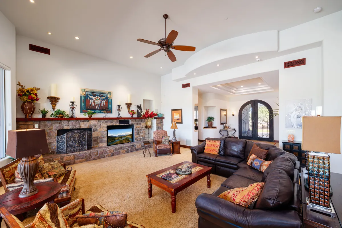 A sunlit living room with a stone fireplace as its focal point, surrounded by comfortable seating and adorned with tasteful artwork and decorative plants. The large windows frame beautiful desert vistas, creating a warm and inviting atmosphere for family movie nights or quiet moments.